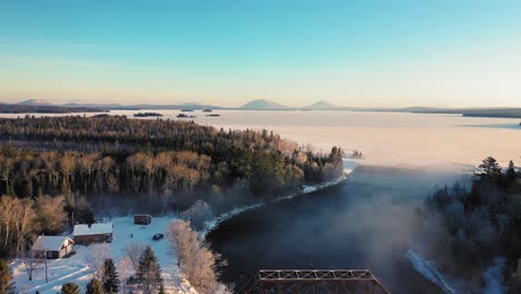 flying high over the mist of a curving winter river past a railroad trestle towards a snow covered frosted lake while a truck drives along the river