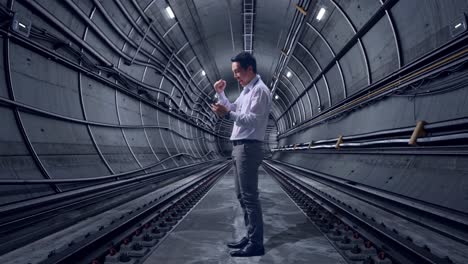 full body side view of an asian male professional worker standing with his phone in underground subway tunnel, he raises his fist up with screaming goal