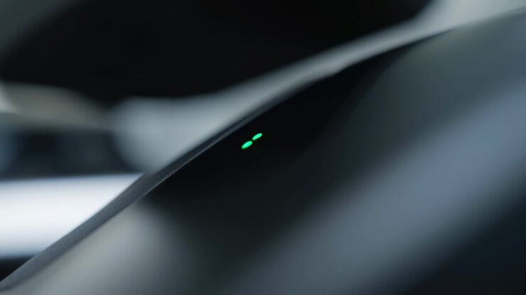Sequenza cronologica in primo piano di finiture interne lucide scure di un'auto al centro-sinistra che mostra un contorno di plastica curvo e una piccola spia luminosa che.