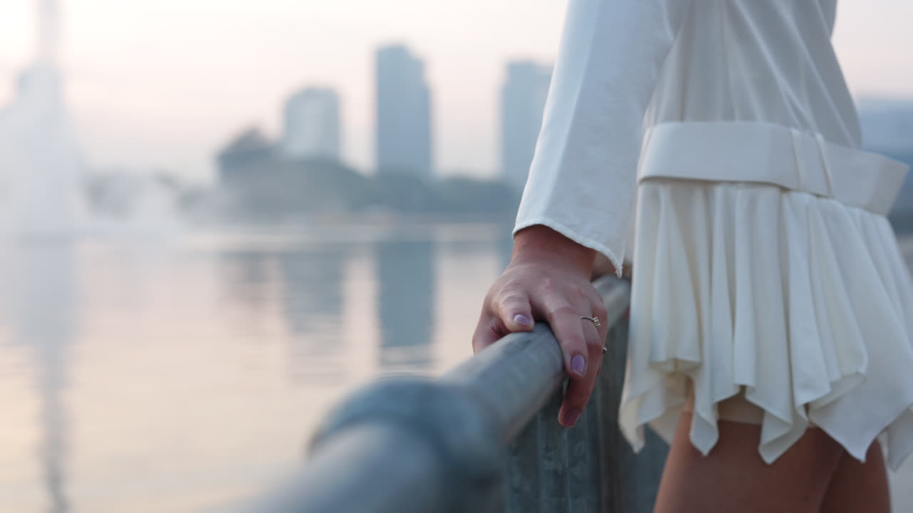 Woman's hand on a railing with a blurred city and water in the background