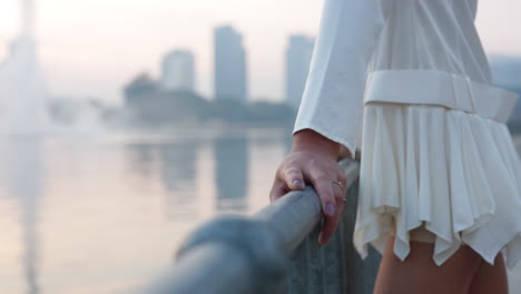 woman's hand on a railing with a blurred city and water in the background
