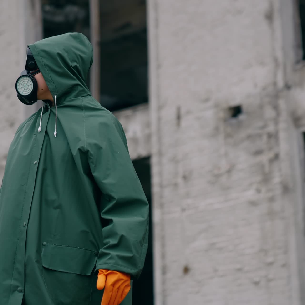 Perplexed survivor in abandoned place. Human in safety uniform and gas mask standing alone and looking to the sides on the background of destroyed buildings