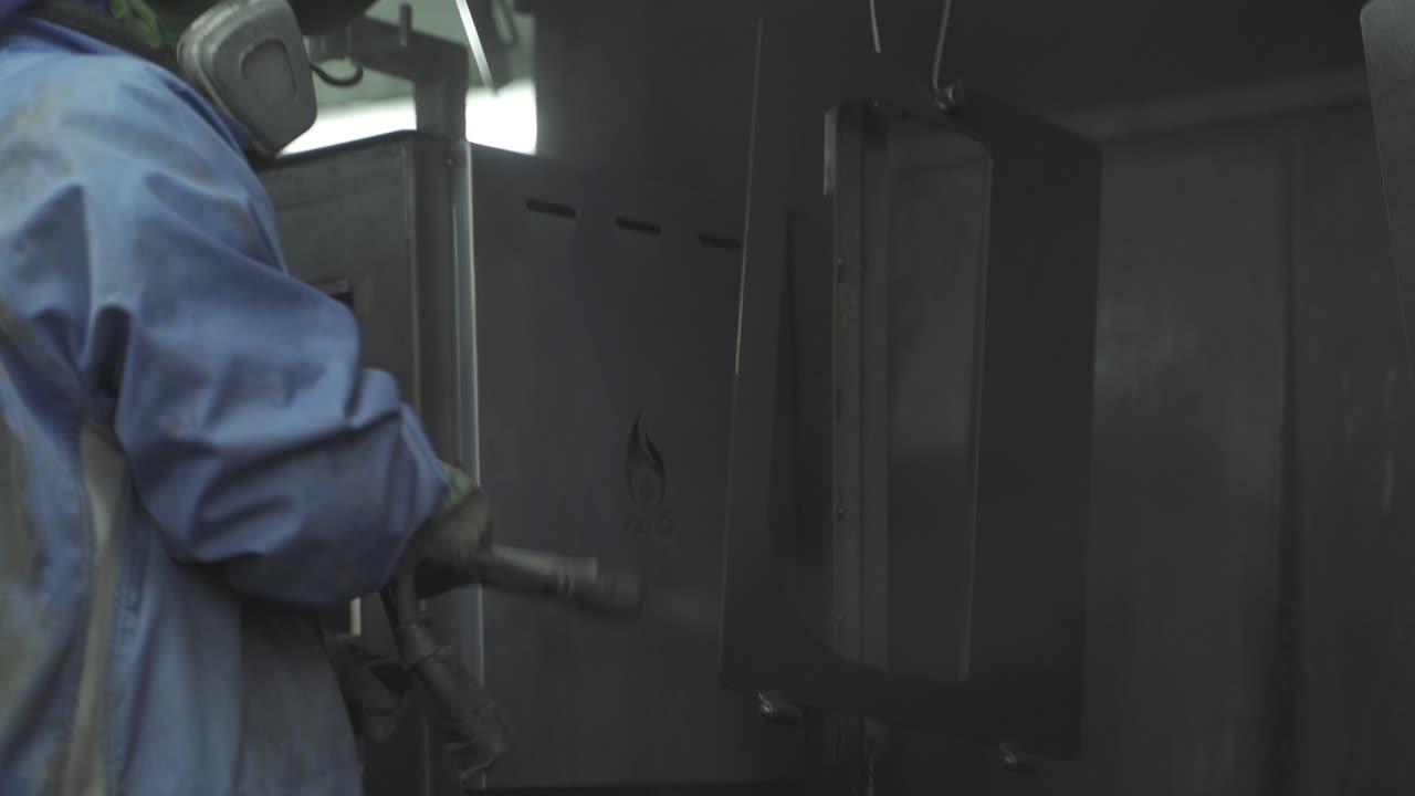 A handheld footage of a factory worker wearing a safety suit while spraying water on steel to clean and cool it down