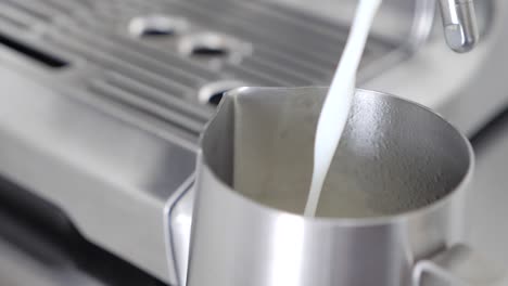 Close-up-slow-motion-of-milk-pouring-into-a-stainless-steel-milk-pitcher-in-order-to-make-a-latte