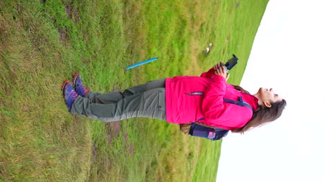 Adventurous-woman-holds-drone-controller-taking-a-break-while-hiking-to-fly-RPAS,-vertical