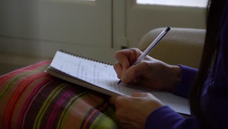 woman sitting on a couch writing notes during her class in the notebook on her lap