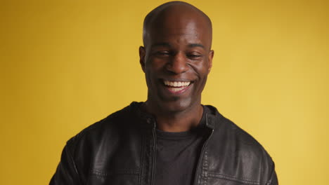 head and shoulders studio portrait of smiling and laughing mature man against yellow background 3