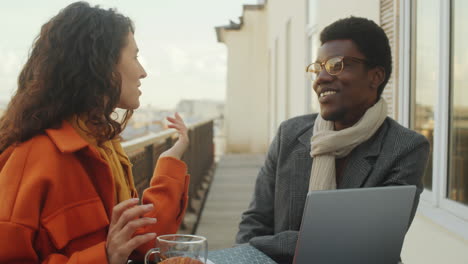 multiethnic colleagues chatting and laughing on rooftop terrace