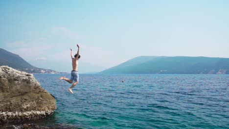 young caucasian man jumping off a rock into the ocean