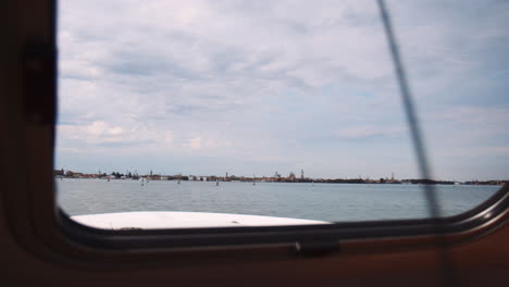 Paisaje-A-Través-De-La-Ventana-De-Un-Barco-Que-Navega-En-La-Laguna-Veneciana-En-Un-Día-Soleado-En-Venecia,-Italia