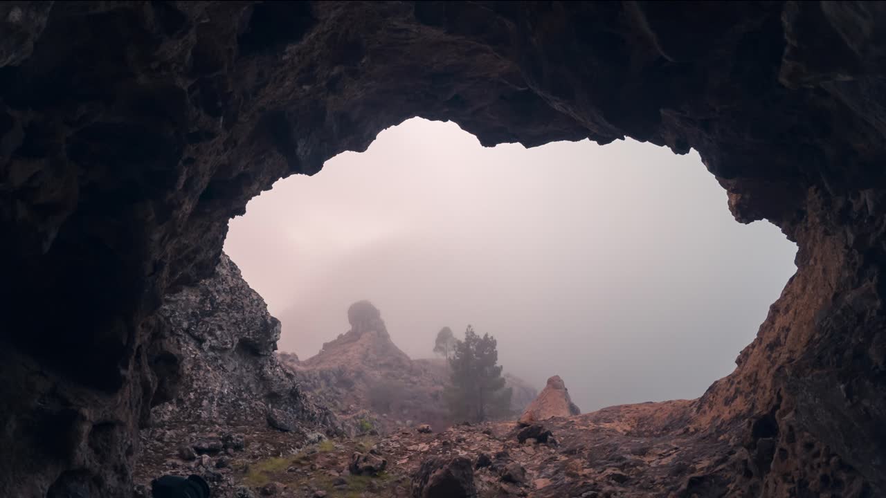 Breathtaking timelapse of Roque Nublo seen from inside a cave, framed by rugged rocks. The misty, cloudy sunset adds a mystical and cinematic touch. Perfect for nature, travel, and adventure projects.