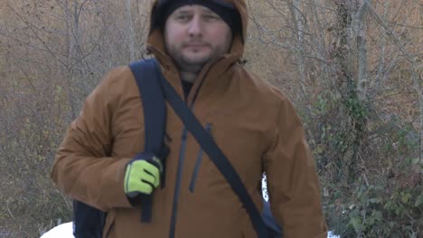 caucasina male wearing orange jacket walking alone in the forest with white snow winter landscape