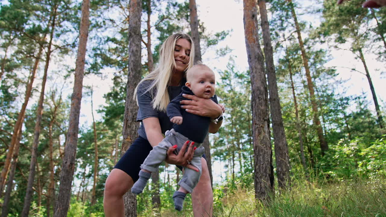 Happy smiling woman waving her cute baby boy. Mom entertaining her child in the nature. Vertical screen.