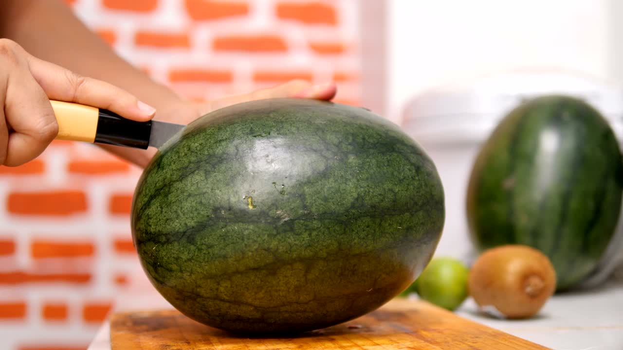 주방 의 나무판 에 있는 수박 의 절반 을 칼 으로 잘라내는 여자 들 의 손