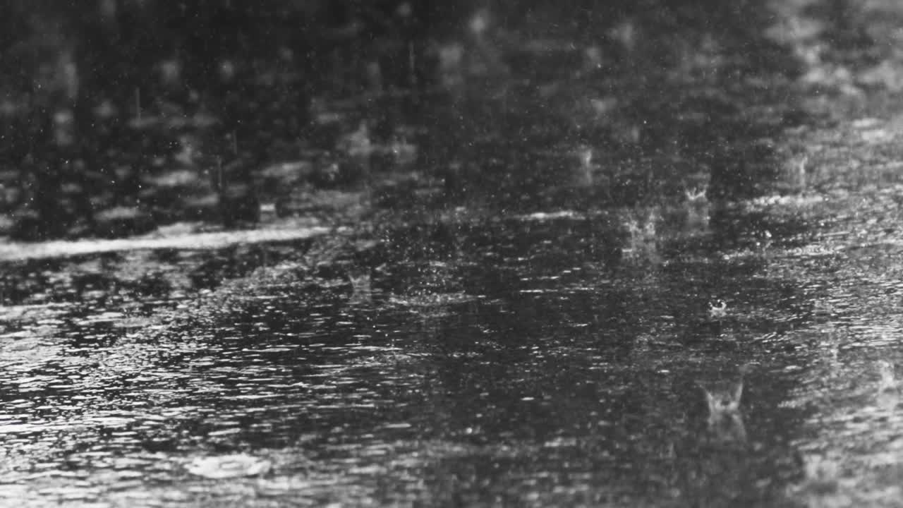 Close up shot of heavy raindrops shattering on an asphalt road in the rain