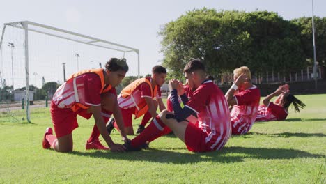 video of diverse group of male football players warming up on field,doing sit -ups