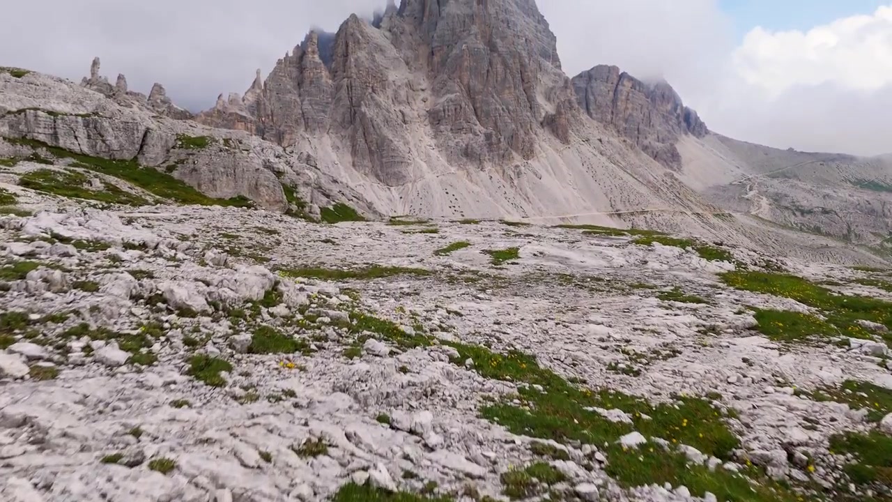 Episkt flygfoto med drönare över Dolomiterna, där moln driver över topparna nära solnedgången i 4K.
