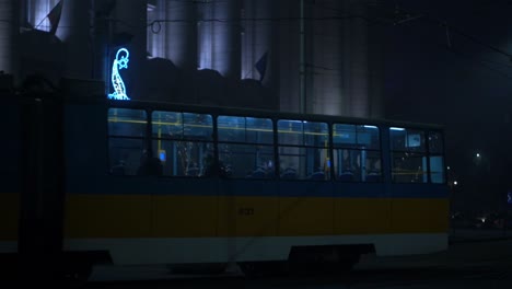 metro rounds corner at night, illuminated by street lights and neon sign