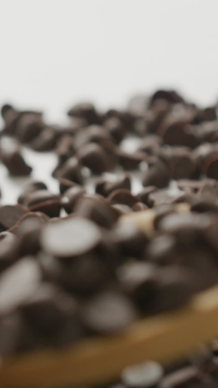 Video of close up of multiple chocolate chip falling on wooden spoon over white background