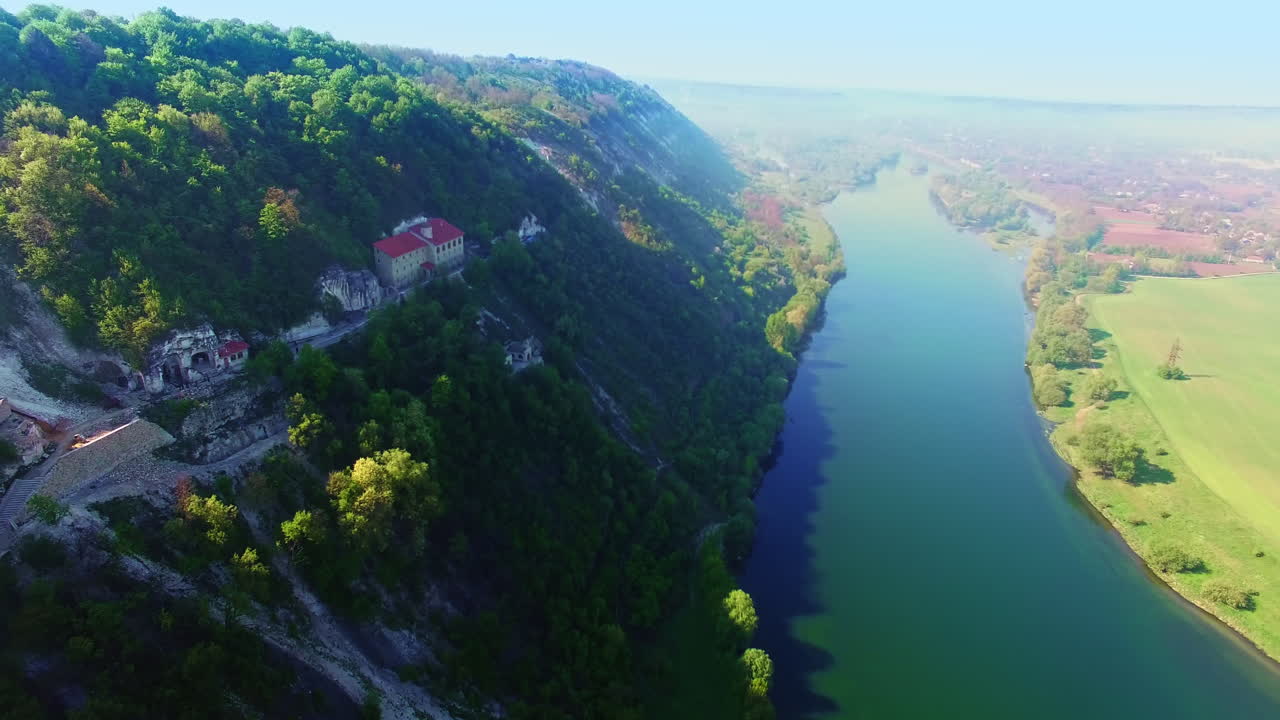Breath-taking view of a mountain with beautiful river at the foot. Rock monastery locating on the slope among the green woods. Aerial perspective.