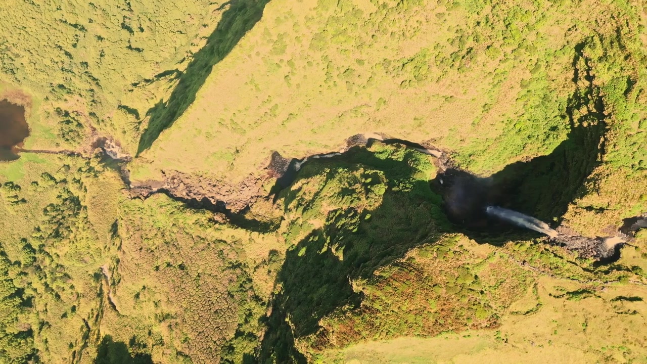 Luftaufnahme enthüllt einen gewundenen Fluss und Wasserfall, der durch üppig grüne Hügel fließt