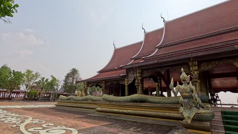 a steady daytime camera pan reveals a traditional lao buddhist temple with ornate dragon statues, intricate architecture, and a serene outdoor courtyard under soft natural light