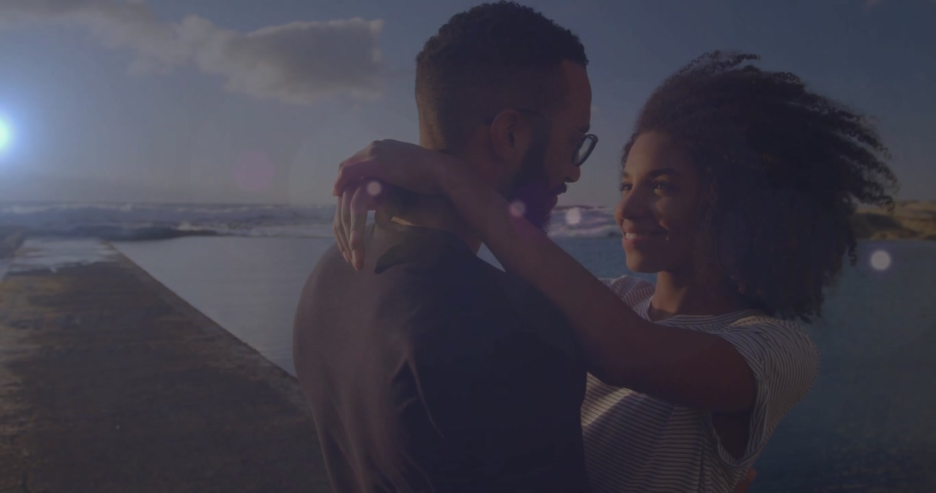 Couple lifting arms embracing on pier sparking soft kiss with lens flare for lifestyle marketing