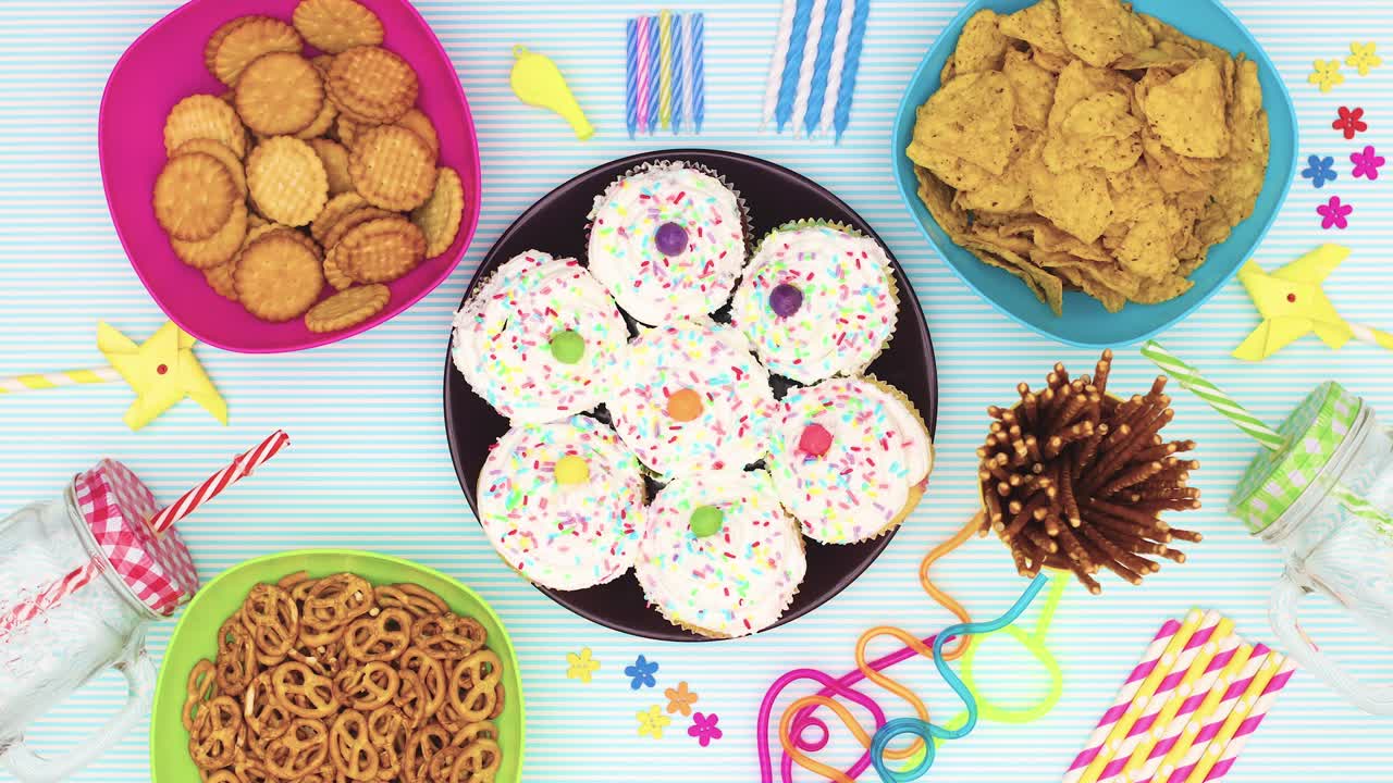 comida y decoraciones de la fiesta de cumpleaños, pasteles, velas, pajitas, comida aparecen en la mesa azul - stop motion