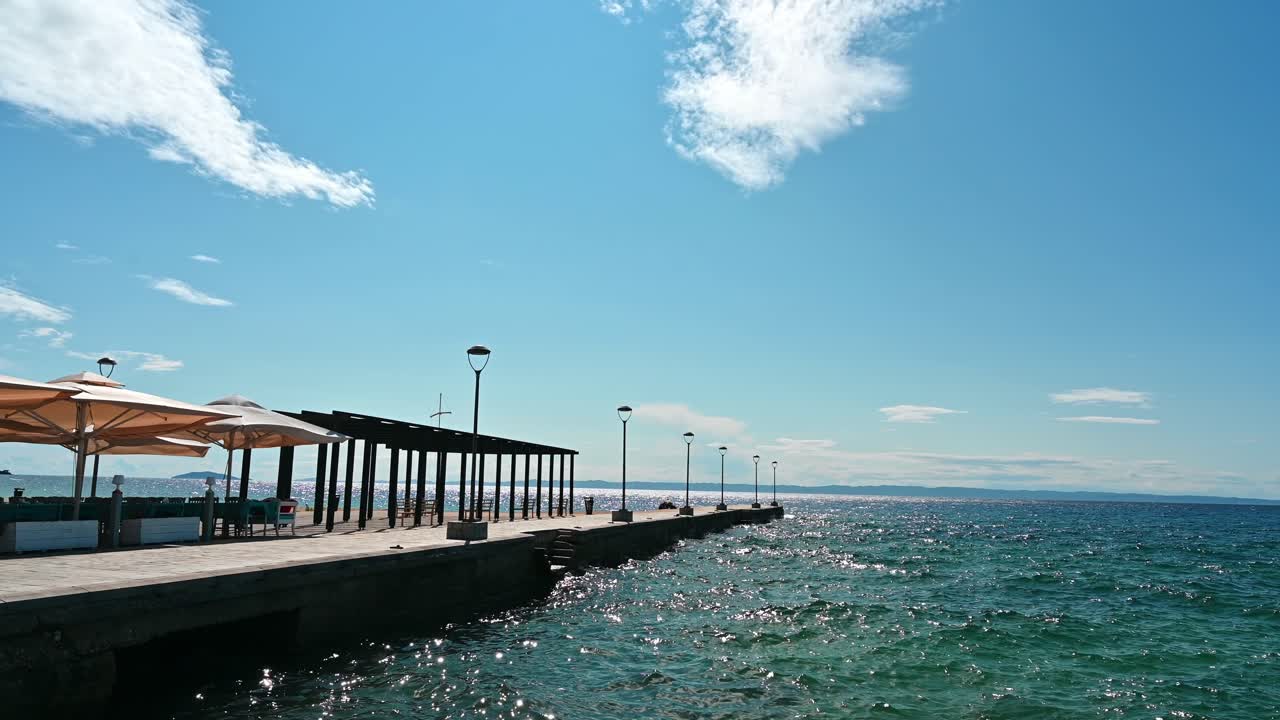 Pier with cafe, umbrellas, gazebo and lamp posts, Aegean sea in Nikiti, Greece