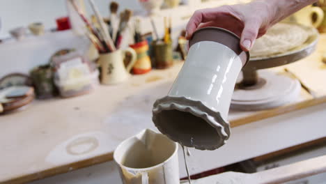 close up of male potter applying glaze to clay vase in ceramics studio