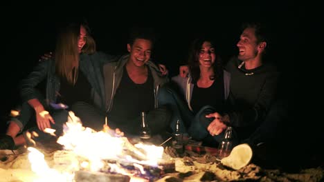 Diverse-group-of-people-sitting-together-by-the-fire-late-at-night-and-embracing-each-other.-Cheerful-friends-talking-and-having