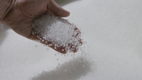 imágenes en cámara lenta de una mano recogiendo y sosteniendo y luego dejando caer pellets de plástico blanco en una fábrica