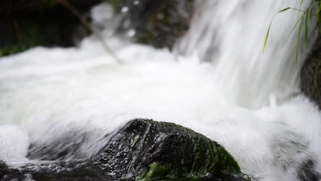 Base-of-a-waterfall-with-the-white,-fresh-water-gushing-over-the-rocks-in-the-stream-below