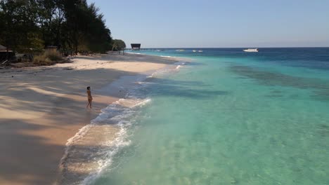 aerial flyover happy woman walkinh along beautiful ocean shore and sandy beach in gili meno