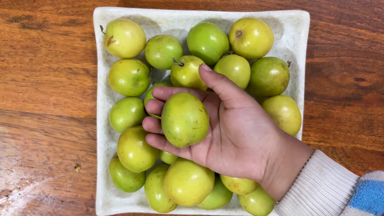 Mano che tiene un frutto di ber verde fresco sopra una ciotola di giuggiole su un tavolo di legno, frutto di stagione sano