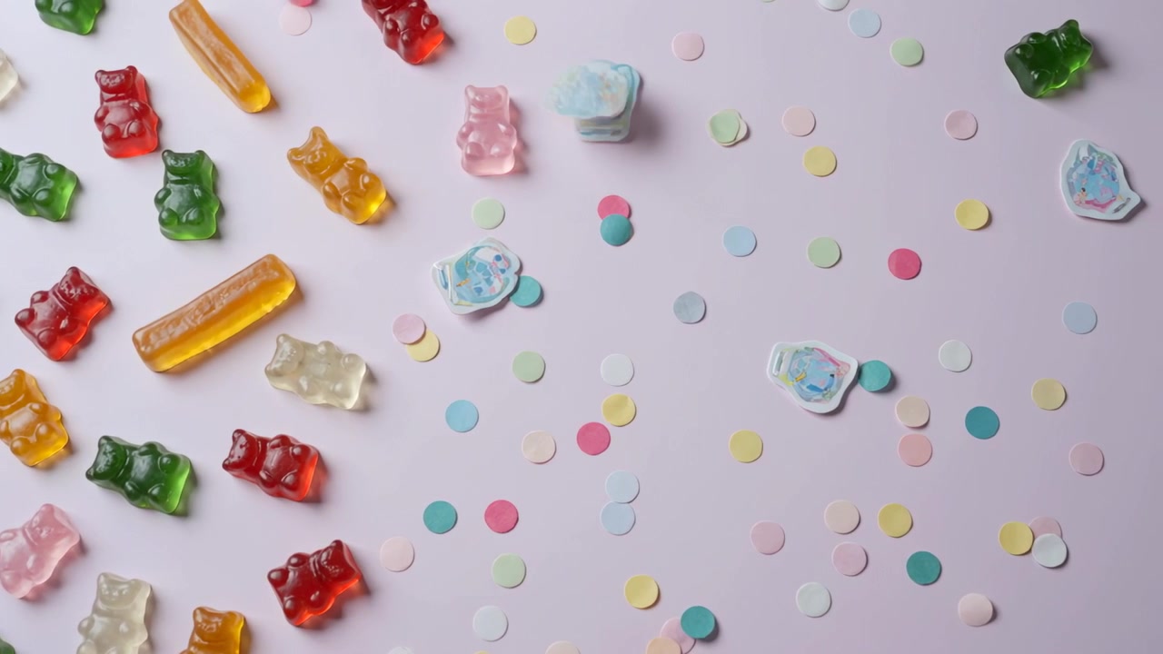 Entering pale blue candy falling onto confetti at pink tabletop, nudging gummy bears, copy space