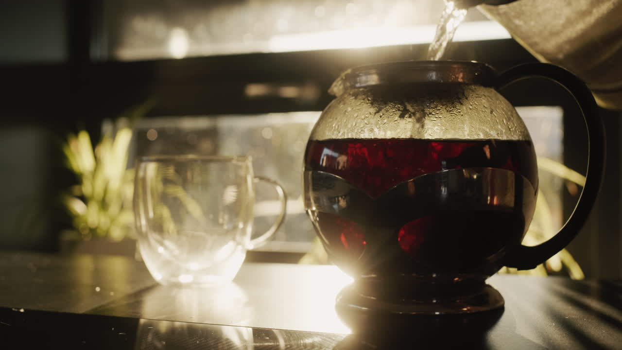 vertiendo el té de una tetera en una taza de vidrio. el sol brilla desde la ventana, ilumina bellamente los platos