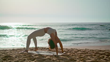 mujer realizando la postura del puente al amanecer. chica practicando yoga asana en la playa.