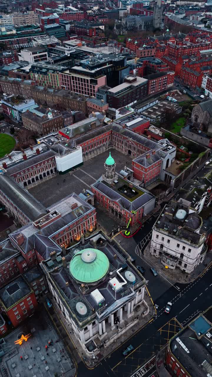 Luftfoto med drone av Dublin Castle i sentrum på en overskyet vinterdag, med irske bygninger nedenfor og trafikkerte veier med biler og busser, samt turister som går rundt.