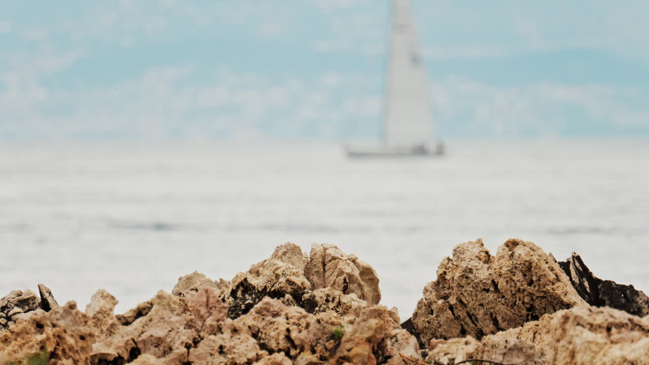 Close up of rugged rocks on the shore with a blurred view of a boat moving on the sea in the background