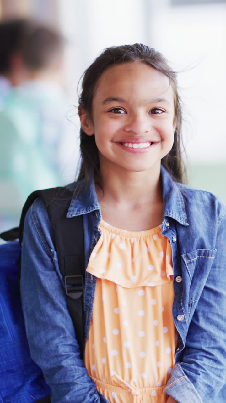 Vertical video of portrait of happy biracial schoolgirl in school