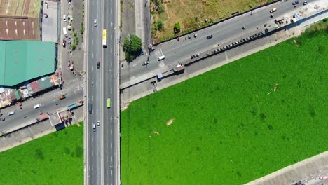 A-top-down-view-shows-the-intercrossing-of-a-lilly-covered-waterway-with-bridges,-roads,-a-shopping-mall-and-apartment-complex