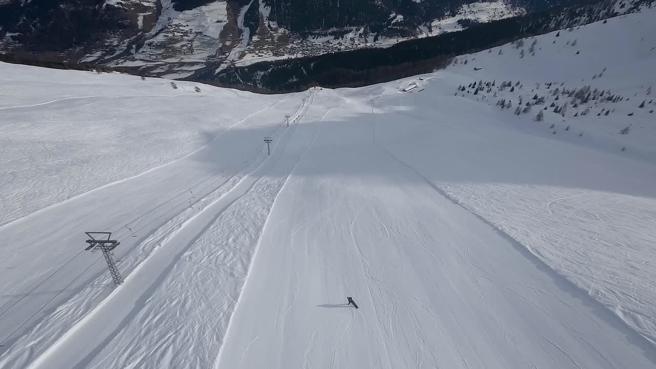 Aerial view of a snowboarder going down an empty wide slope with wonderful mountain range in background