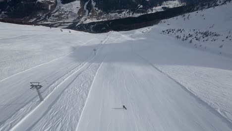 Aerial-view-of-a-snowboarder-going-down-an-empty-wide-slope-with-wonderful-mountain-range-in-background