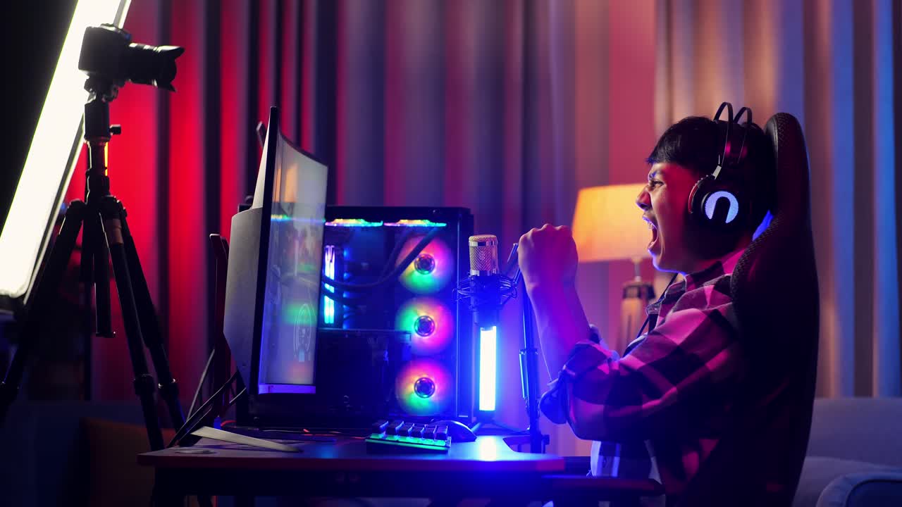 vista lateral del niño asiático streamer gritando gol celebrando el juego ganador a través de la red en la computadora personal. videojuego de transmisión en vivo, escritorio iluminado por luz de tira de led rgb