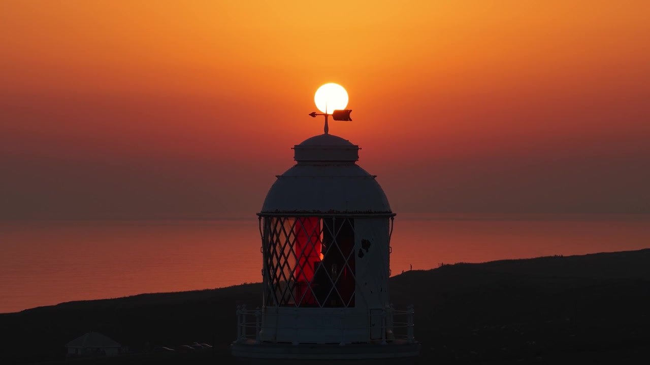 Riprese aeree cinematografiche con drone che sorvolano il faro di Nash Point al tramonto, rivelando scogliere drammatiche, cieli dorati e la suggestiva costa del Galles del Sud.