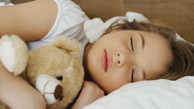 Close-up view of cute blonde little girl sleeping on the bed while hugging her teddy bear in the morning