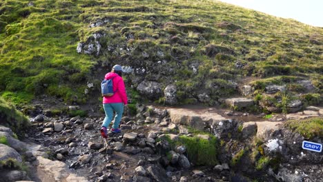 mujer cruzando un pequeño arroyo con rocas, continuando la caminata en el lago sorvagsvatn