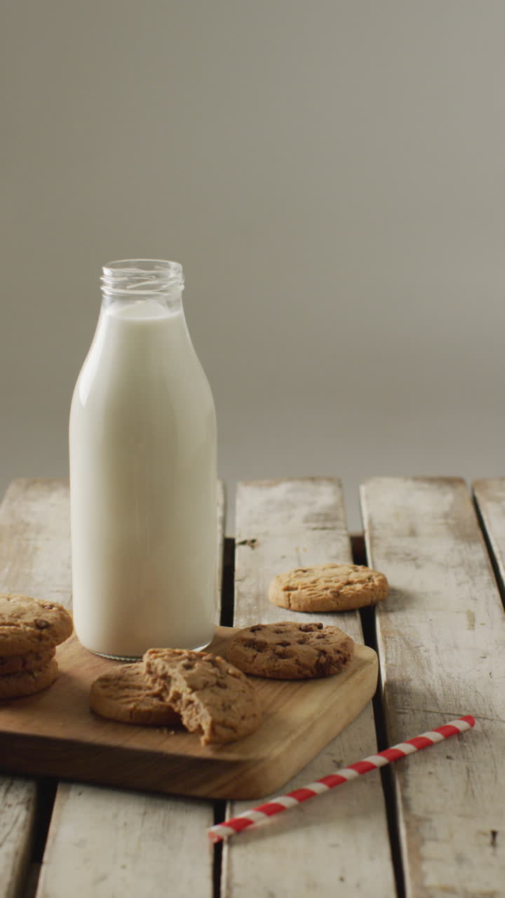 video vertical de galletas de chispas de chocolate y botella de leche en tabla de cortar y fondo de madera