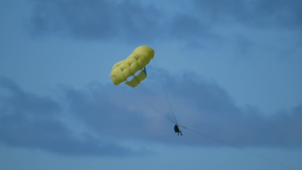 una pareja haciendo parapente colgando de un paracaídas amarillo en una isla tropical